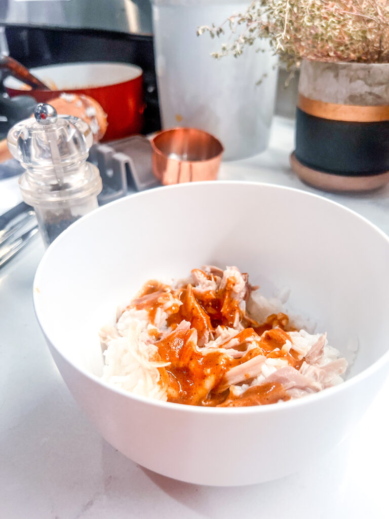 quick and easy homemade enchilada sauce poured over white rice and chicken in a white bowl on a granite countertop with decor behind it