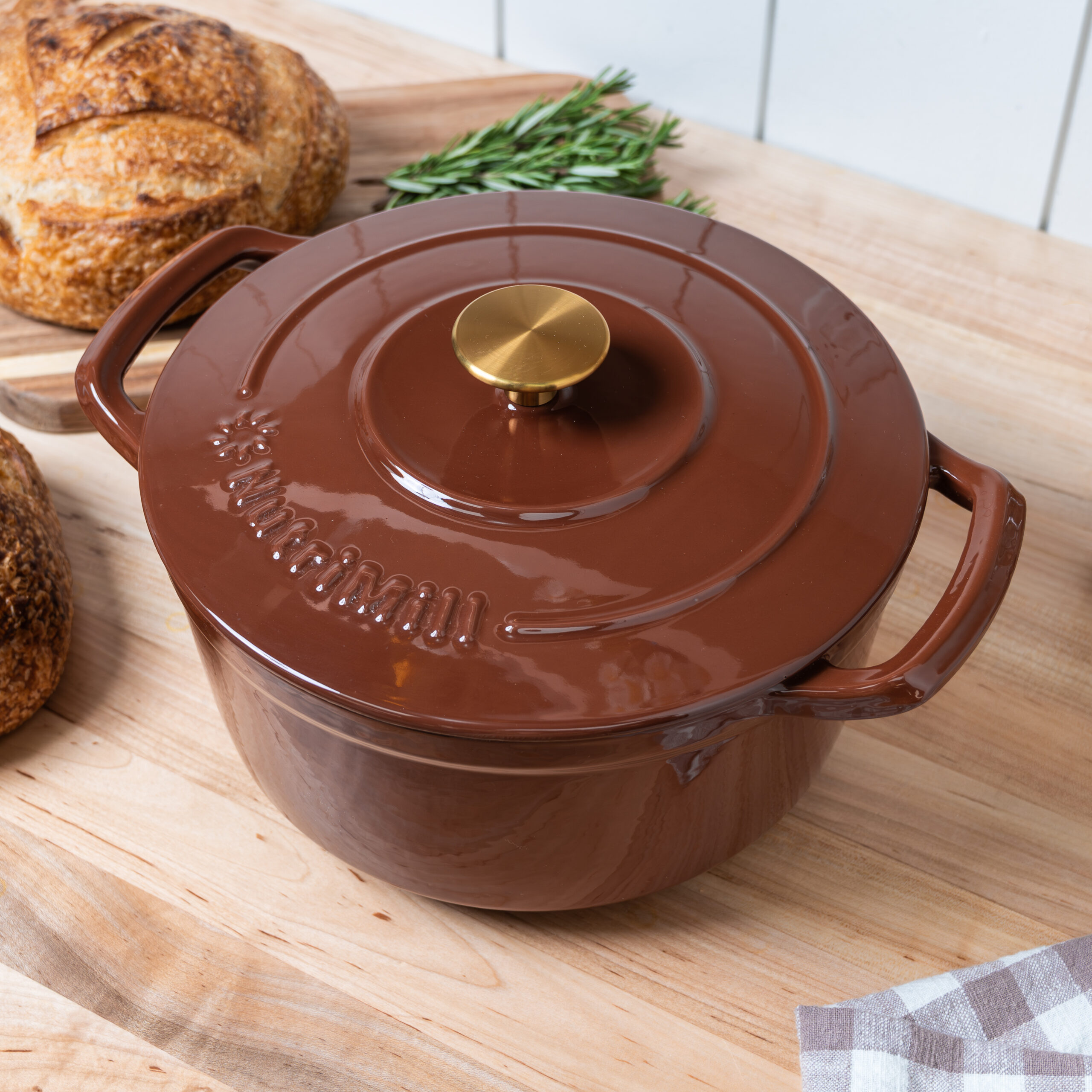 nutrimill enameled cast iron dutch oven in cinnamon color with a brass knob on the lid; the dutch oven is sitting on a wooden countertop
