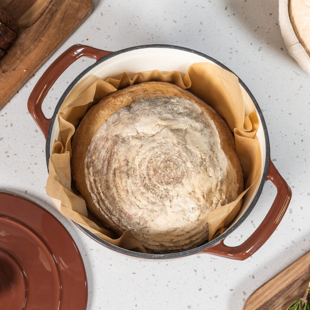 sourdough bread in parchment paper in a dutch oven colored cinnamon on top of a white countertop