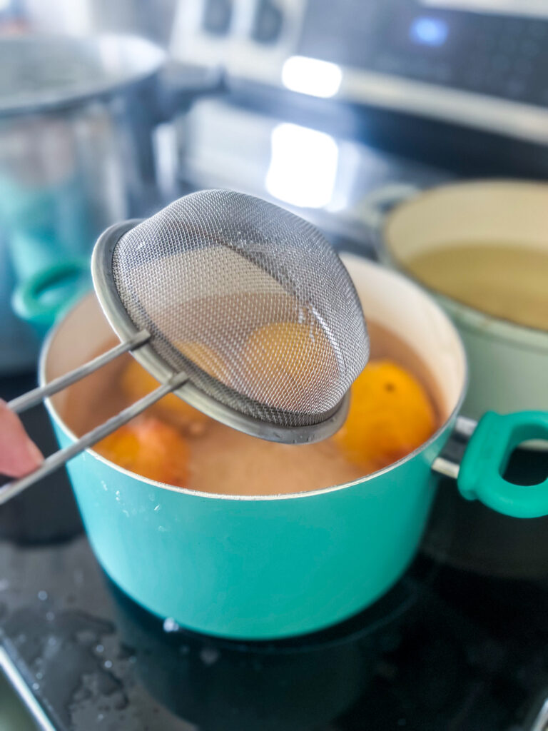 a stainless steel mesh strainer putting peaches into a teal pot of boiling water to blanch them
