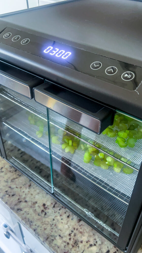 food dehydrator running with a timer saying 3 hours and inside is two trays of cut celery