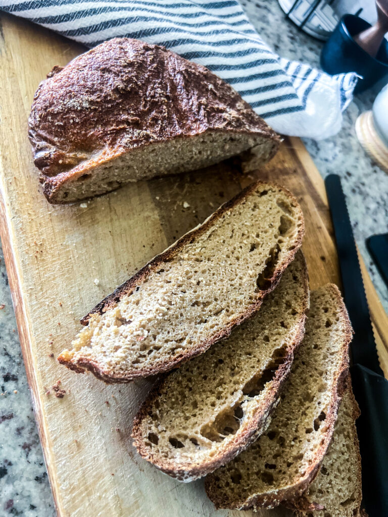 Freshly milled whole wheat bread on a wooden cutting board with an all black bread knife and a linen striped bread towel