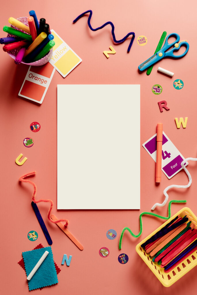 a peach colored table with several colorful art supplies on it like pipe cleaners, scissors, markers, and a blank piece of white paper