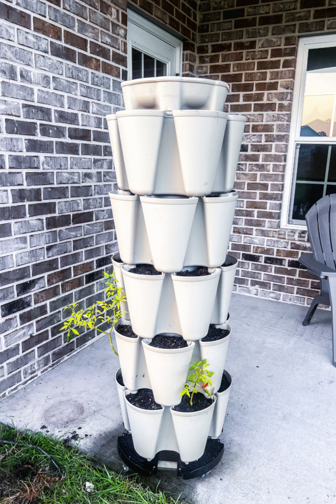 vertical planter tower with soils and seeds started on a cement patio with a brick house in back