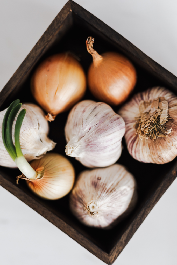 a square wooden bowl with fresh garlic and onions