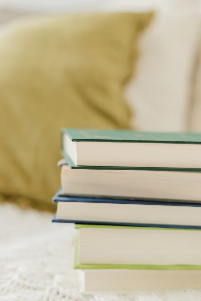 pile of books on top of white blanket with army green pillow in the background